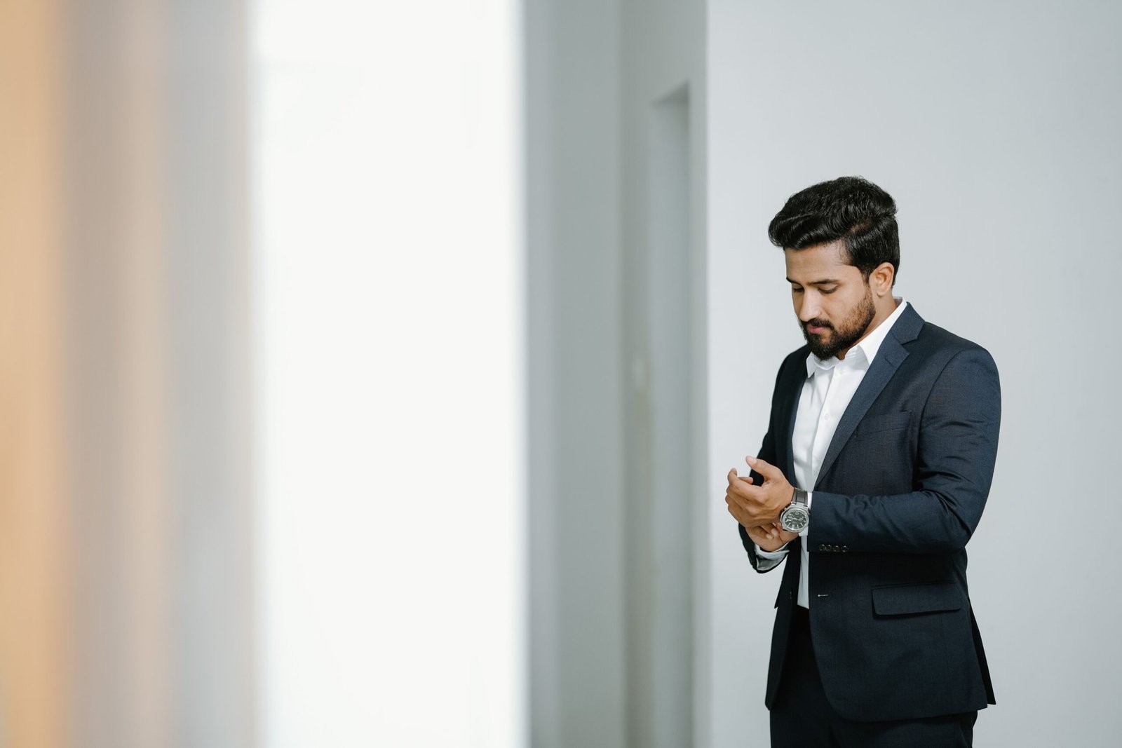 Elegant South Asian man in a suit adjusting his sleeves indoors.